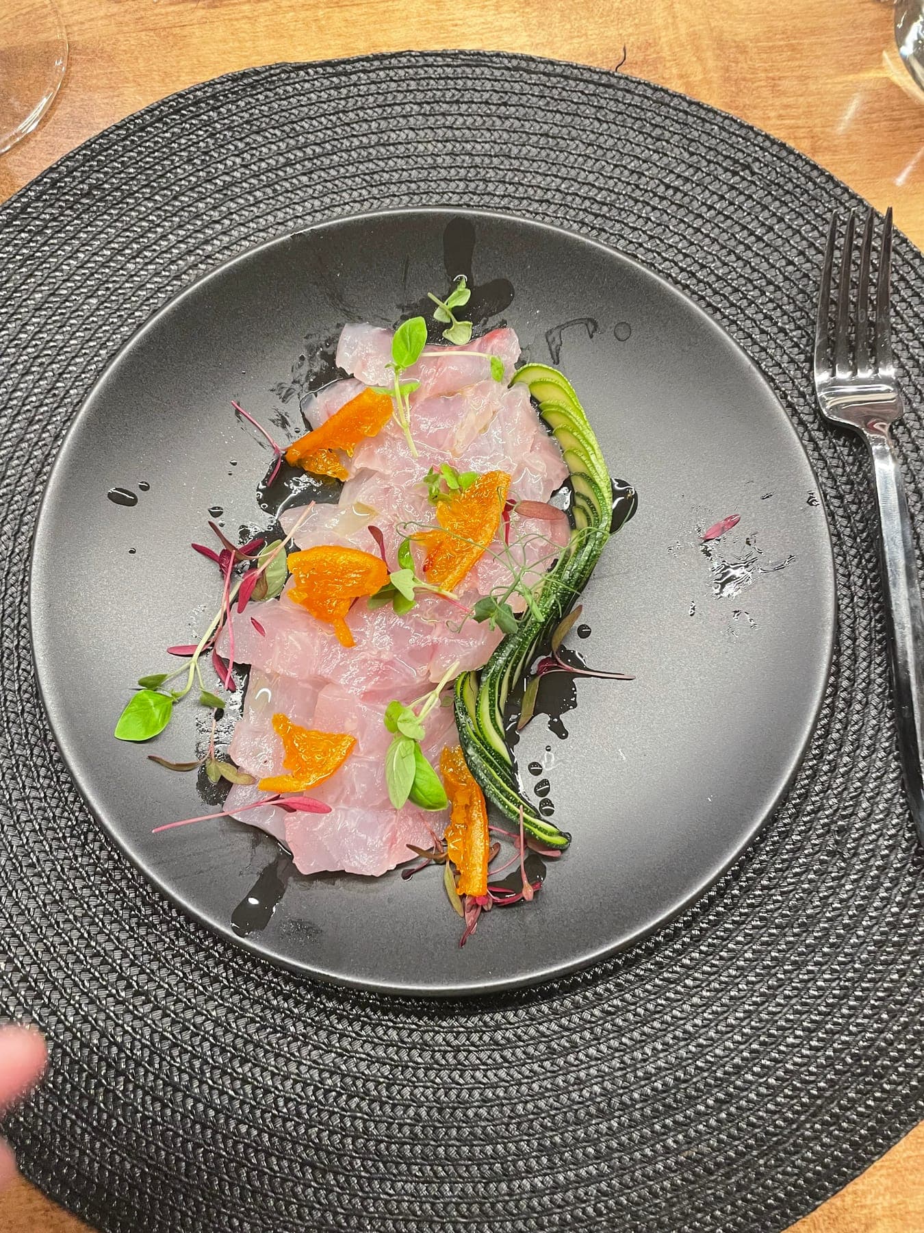 Fish crudo with citrus and charred scallion on a black plate