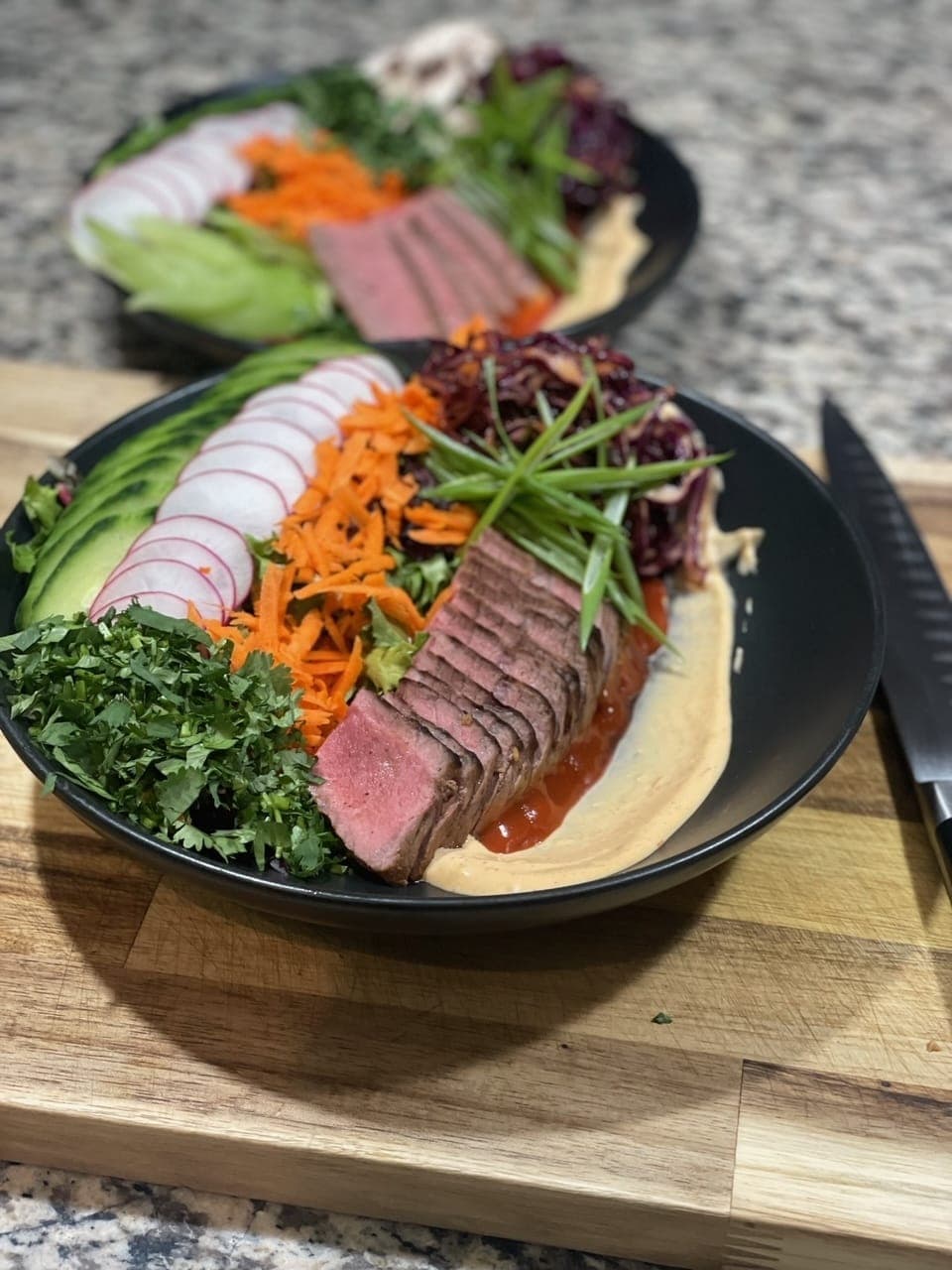 Sliced steak over hummus with pickled vegetables and greens